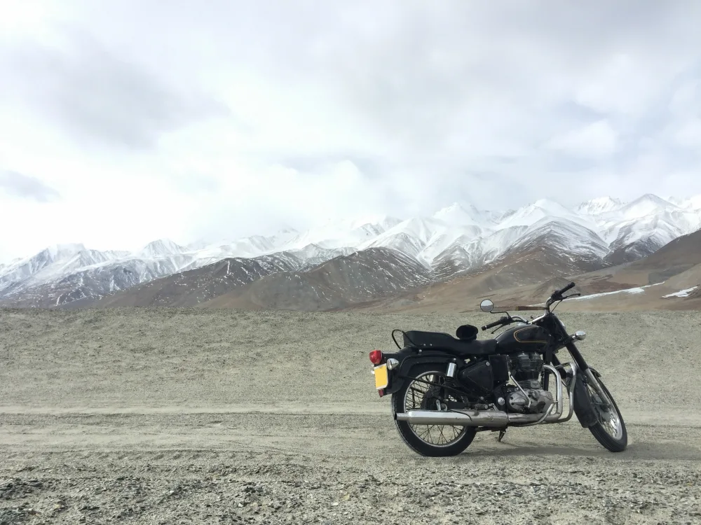 Motorcycle parked on a remote mountain road in Ladakh with snow-covered peaks in the background
