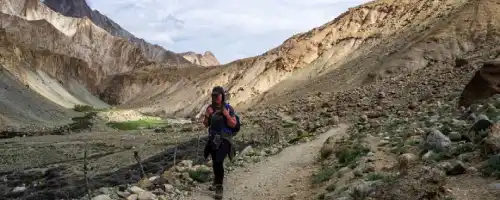 Trekker hiking on a narrow trail through a rocky mountain valley.