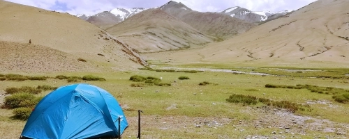 Blue tent pitched in a grassy valley with mountains in the background.