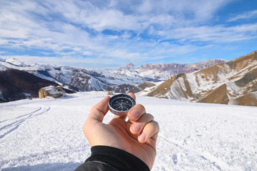Hand holding a compass with snowy mountains in Ladakh in the background.