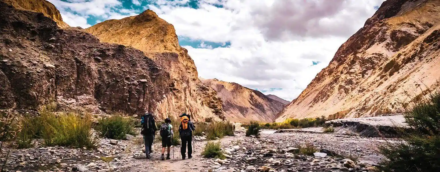 Three trekkers walking through a rocky mountain valley.