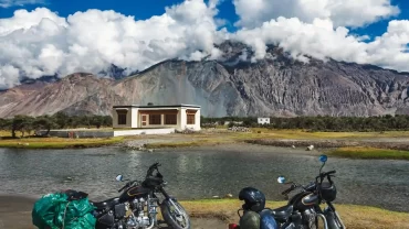 Motorcycles parked beside a river in Ladakh with mountains in the background.