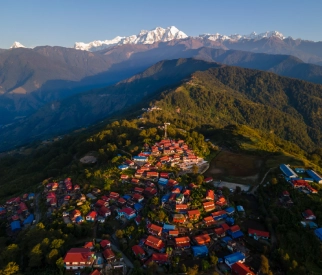 Aerial view of a colorful hill town surrounded by lush forests and snow-capped Himalayan mountains in Sikkim.