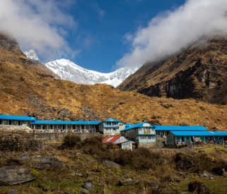 Mountain village with blue-roofed buildings set against snow-capped Himalayan peaks in Sikkim.