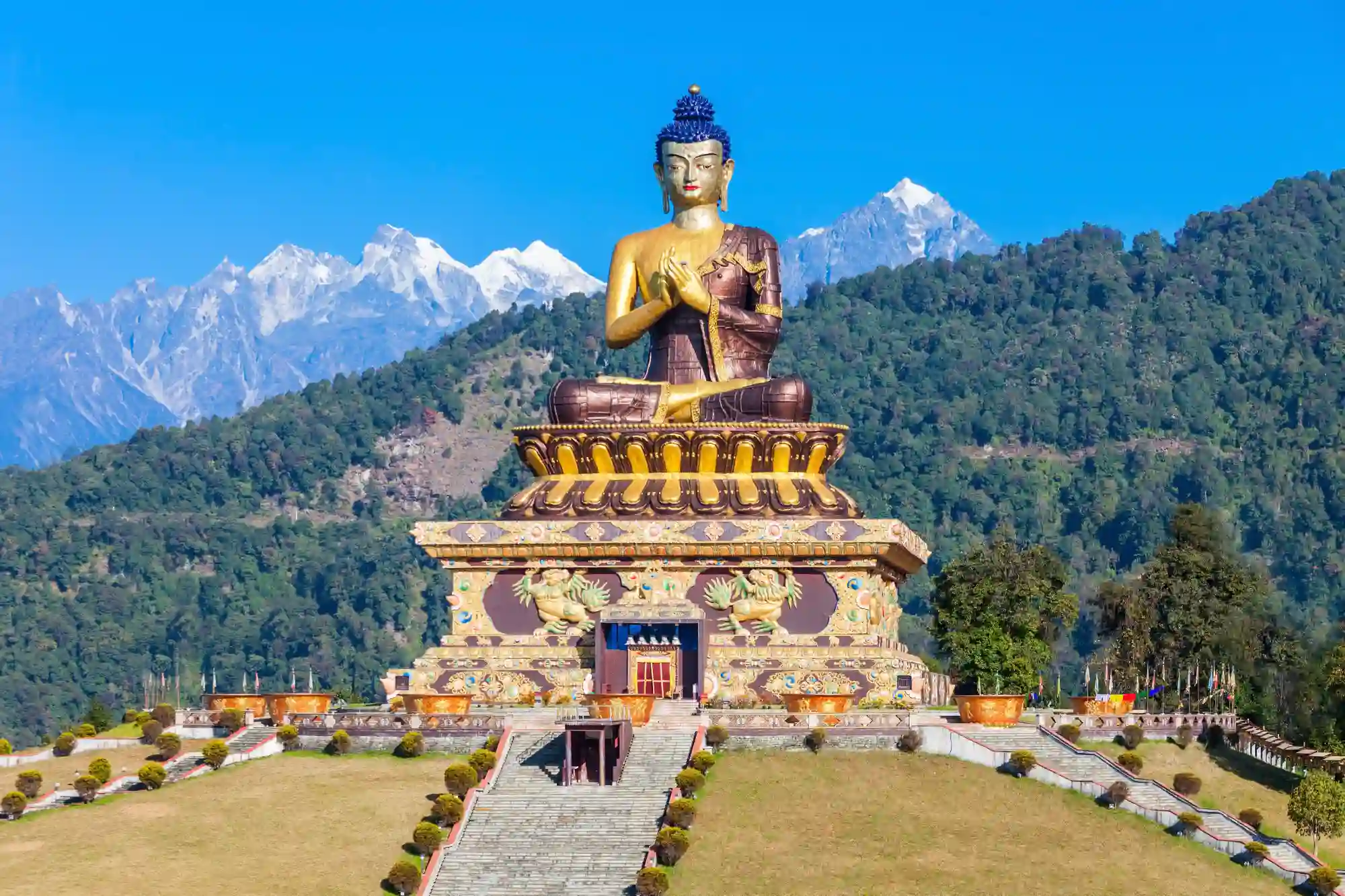 Giant Buddha statue with snow-capped Himalayan mountains in the background.