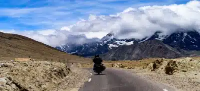 Motorcyclist riding on a remote road in Ladakh with dramatic mountain views.