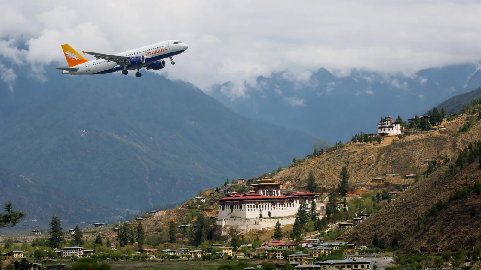 The first time I flew into Paro, I actually gasped out loud. One moment the plane was threading between brown ridges close enough to count the pines, the next it banked hard, dipped a wing toward a monastery on a cliff, and dropped into a valley so green and quiet it felt like the aircraft had accidentally time-traveled. That’s Bhutan for you. Getting here isn’t as breezy as booking a weekend in Bangkok — but it’s genuinely part of the story. Most people reach Bhutan one of two ways: flying into Paro International Airport, or crossing overland from India. Neither is “difficult” once you know how the pieces fit — the visa, the permits, the Sustainable Development Fee, the airline choices. This guide walks you through both routes exactly the way I’d explain it to a friend over chai, plus the small details that make the journey smoother. By Air: Flying Into Bhutan Paro International Airport (PBH) sits at 7,300 ft, squeezed into a narrow valley ringed by 18,000 ft peaks. Only a handful of pilots in the world are certified to land here, and once you've watched a wingtip clear a hillside by what feels like an arm's length, you'll understand why. It also means only two airlines operate scheduled flights: Even the airport wears traditional dress — Paro's terminal is arguably the prettiest in Asia. Drukair — Royal Bhutan Airlines, the national carrier. Bhutan Airlines— the private alternative, often slightly cheaper. Between them, they connect Paro with a small but useful set of cities: India: Delhi, Kolkata, Bagdogra, Guwahati, Mumbai (seasonal) Southeast Asia: Bangkok, Singapore Neighbors: Kathmandu, Dhaka Flight times are short — Delhi is about 2h 30m, Kolkata roughly 1h, Bagdogra a quick 40 minutes, Bangkok around 3h 30m. Return fares swing wildly with season: expect roughly ₹18,000–₹35,000 (US$220–$420) from Indian metros and US$450–$700 from Bangkok or Singapore. Book early for spring and autumn — the good windows sell out weeks in advance. On the Kathmandu–Paro leg, request a left-side window seat. On a clear morning you'll see Everest, Makalu, Kanchenjunga, and Jomolhari lined up like a Himalayan hall of fame. Bring a real camera; phone photos through the scratched cabin window never quite do it justice. The terminal itself is charming — hand-painted wooden facades, no glass towers, no aggressive duty-free maze. You’ll clear immigration in twenty minutes and step outside straight into pine-scented mountain air. Paro town is a 15-minute drive; Thimphu is about an hour. BhutanTour Packages By Train: Reaching Bhutan via Indian Railways Bhutan has no railway network, so you cannot travel directly into the country by train. The easiest option is to take a train to one of the nearby railway stations in India and continue by taxi or bus to the Bhutan border. Even the airport wears traditional dress — Paro's terminal is arguably the prettiest in Asia. Best Railway Stations Near Bhutan Hasimara (West Bengal) – Quieter, useful if you're coming from central Assam or Kaziranga. New Jalpaiguri (NJP), Siliguri – Around 150 km from Phuentsholing (4–5 hours by road). NJP is one of the best-connected railway stations in eastern India, with direct trains from Delhi, Kolkata, Guwahati, Mumbai, Chennai, and other major cities. Alipurduar Junction – Approximately 60 km from the border, offering another convenient option with regular taxi services to Phuentsholing. Once you arrive at any of these stations, you can hire a private taxi or board a shared cab or bus to Phuentsholing, Bhutan's busiest land entry point. Approximate Travel Time Route Duration Hasimara → Phuentsholing 30 Minutes NJP → Phuentsholing 4–5 Hours Alipurduar → Phuentsholing 1.5–2 Hours Cross the border between 9:30 and 11:00 AM on a weekday. The immigration office opens at 9, the early rush clears by 9:30, and lunch-hour queues haven't built up yet. Avoid Saturdays — half of Jaigaon seems to be crossing over to shop. From Phuentsholing to Thimphu is around 170 km but plan for 6 hours — the road climbs from 300 m to 2,300 m through switchbacks, waterfalls, and fog-drenched pine forest. Shared taxis and prepaid cabs are easy to find; the Bhutan Post bus is cheapest if you’re not in a hurry. By Road: Entering via India There are three official land borders into Bhutan, all from India: Even the airport wears traditional dress — Paro's terminal is arguably the prettiest in Asia. Phuentsholing (from West Bengal) — the main gateway, ~170 km from Bagdogra airport / Siliguri, roughly a 4–5 hour drive. Gelephu (from Assam) — quieter, useful if you're coming from central Assam or Kaziranga. Samdrup Jongkhar (from Assam) — the far eastern entry, ideal if you're finishing a Northeast India loop and want to exit through east Bhutan. Phuentsholing is where most road travelers cross, and the contrast at the border is genuinely surreal. On the Indian side, Jaigaon is chaos in the best Indian tradition — honking trucks, tangled wires, vendors yelling over Bollywood remixes. Walk 30 seconds under the Bhutan Gate and suddenly the traffic moves in orderly lines, no one leans on a horn, and the shopkeepers are wearing gho and kira. It's like stepping through a portal. For Indian nationals, this crossing is refreshingly simple: no visa required. You just need either a valid passport (min. 6 months) or a Voter ID card, plus two passport photos. You'll get a free entry permit from the Immigration Office right next to the gate. Cross the border between 9:30 and 11:00 AM on a weekday. The immigration office opens at 9, the early rush clears by 9:30, and lunch-hour queues haven't built up yet. Avoid Saturdays — half of Jaigaon seems to be crossing over to shop. Even the airport wears traditional dress — Paro's terminal is arguably the prettiest in Asia. From Phuentsholing to Thimphu is around 170 km but plan for 6 hours — the road climbs from 300 m to 2,300 m through switchbacks, waterfalls, and fog-drenched pine forest. Shared taxis and prepaid cabs are easy to find; the Bhutan Post bus is cheapest if you’re not in a hurry. Perfect Tip : First-time visitors, honeymooners, photographers, trekkers, and luxury travelers looking to experience Bhutan’s most beautiful season with ideal weather and unforgettable Himalayan scenery. This Bhutan Travel Guide helps you choose the perfect season for an unforgettable journey through the Land of the Thunder Dragon. Mode Best For Entry Point Travel Time Approx. Cost Air Fastest & Most Comfortable Paro International Airport 40 min–3.5 hrs ₹18,000–₹35,000+ Train Budget Travellers Hasimara / NJP / Alipurduar 30 min–5 hrs (Road Transfer) Train Fare + Taxi Road Flexible & Scenic Phuentsholing, Gelephu, Samdrup Jongkhar 4–6 hrs Taxi / Bus Which Route Should You Choose? Quick decision framework, based on where you're starting: ✈️ Delhi / Kolkata / Short Trip Fly directly to Paro. You'll spend less time in transit than the drive from Bagdogra alone. 🚗 Budget Road-Tripper Fly into Bagdogra, cross at Phuentsholing. Cheapest option, and the drive up is unforgettable. 🗺️ Northeast India Combo Pair Kaziranga or Tawang with Bhutan via Gelephu or Samdrup Jongkhar. ❤️ The Romantic Combo Fly in, road out (or vice versa). You get the aerial reveal and the slow-earned descent. Personally, my favorite is flying in and driving out. The arrival by air is jaw-dropping, and leaving overland gives you a final slow look at the country as you unwind from mountain calm back into Indian energy. It feels like a proper goodbye. Visa & Permit Requirements Foreign visitors apply online in advance; Indians can walk up and get a permit at the border. Foreign nationals (most passports) Apply for an e-visa online through the official Bhutan Department of Immigration portal. You'll need to upload a passport scan and a recent passport-size photo, provide your travel itinerary, and pay the visa fee (approximately ₹3,500–₹3,700) along with your Sustainable Development Fee (SDF) in advance. Visa applications are typically processed within 5 working days. Since 2022, independent travel has been permitted, so booking through a licensed tour operator is no longer mandatory. Indian, Bangladeshi & Maldivian nationals No visa. Just an entry permit issued on arrival (free for Bhutan, but the SDF still applies, at a lower rate). Bring passport or Voter ID, two photos, and a copy of your hotel booking. The Sustainable Development Fee (SDF) This is Bhutan's famous "high-value, low-impact" tourism policy in action. The Sustainable Development Fee (SDF) is currently ₹8,700 per adult per night (approximately US$100) for most foreign nationals, while Indian citizens pay ₹1,200 per person per night. The revenue helps fund Bhutan's free healthcare, education, environmental conservation, and cultural preservation—meaning your contribution directly supports the country's sustainable development while you enjoy its pristine landscapes and unique heritage. Once you're inside Bhutan, if you want to travel beyond Thimphu and Paro (Punakha, Bumthang, Phobjikha, etc.) you'll need a route permit, issued free at the Immigration Office in Thimphu. Your hotel or driver usually handles this in an hour. Discover the Beauty of Bhutam Bhutan Honeymoon Bhutan Honeymoon Bhutan Honeymoon Package 7 Nights 8 Days 12 Reviews 7 Nights 8 Days from ₹50000 Bhutan tour packages Triphills.com Bhutan tour packages Triphills.com Bhutan Honeymoon Tour Package 6 Nights 7 Days 10 Reviews 6 Nights 7 Days from ₹48,999 Best Time to Travel & Practical Tips Bhutan has two clearly dominant seasons for visitors: Spring (March–May): Rhododendrons in bloom, mild days, the legendary Paro Tshechu in late March or early April. Autumn (September–November): Crystal-clear mountain views, harvest color, and the huge Thimphu Tshechu in September–October. Everything else worth knowing, in bullets: Currency: Ngultrum (Nu), pegged 1:1 with the Indian Rupee. INR notes up to ₹100 are widely accepted; carry small denominations. Connectivity: Pick up a local TashiCell or B-Mobile SIM at the airport for a few hundred rupees — 4G is decent in towns, patchy in valleys. Packing: Layers, a proper rain shell, decent hiking shoes if you plan to trek to Tiger's Nest, and modest clothing for temples (long pants, covered shoulders). Etiquette: Remove shoes and hats at temples, walk clockwise around stupas and prayer wheels, and please don't point at religious icons. Cash: ATMs work in Thimphu and Paro but can be unreliable; carry backup cash. For a complete overview of Bhutan’s famous sightseeing spots and offbeat destinations, check out our comprehensive Bhutan tourist places guide. Final Thoughts : Reaching Bhutan is its own miniature adventure — a plane ride that feels closer to flying than any other, or a slow drive up out of the plains into pine and prayer flags. Either way, by the time you're standing in front of Tiger's Nest with the wind at your back, the paperwork and the border queues have already faded into a story you'll tell for years. Pick your route, book your window seat (left side, remember), and start planning. Bhutan is waiting on the other side of the mountains. Want this itinerary tailored to your dates? Share your travel window and we will send you a personalised plan within 24 hours. Get a Free Quote → Things travellers actually ask Do Indians need a visa for Bhutan? No. Indian nationals only need a passport or Voter ID card plus a free entry permit issued on arrival at Paro airport or the Phuentsholing border. The SDF (₹1,200 per adult per night) still applies. Which is better — flight or road? How much does the Sustainable Development Fee cost? Can foreigners enter Bhutan by road? Is Bhutan cold in winter?